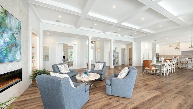 living room featuring beam ceiling, a tile fireplace, ornate columns, coffered ceiling, and light wood-type flooring