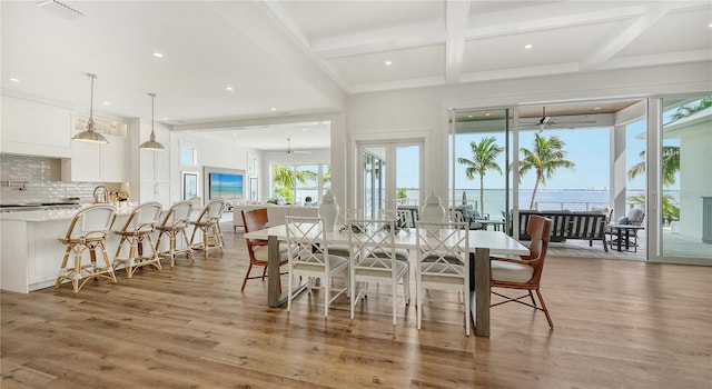 dining space with beam ceiling, ceiling fan, a water view, and light wood-type flooring