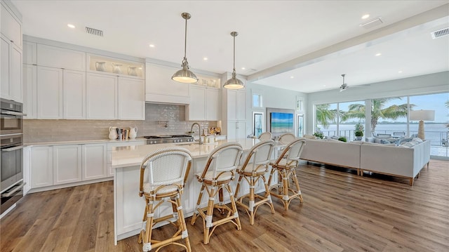 kitchen with white cabinets, a center island with sink, hanging light fixtures, hardwood / wood-style flooring, and ceiling fan