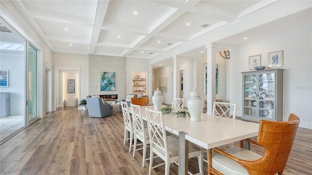 dining space with coffered ceiling, light wood-type flooring, a fireplace, beam ceiling, and decorative columns