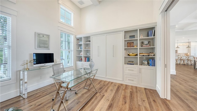 home office featuring light hardwood / wood-style flooring, beamed ceiling, and a high ceiling