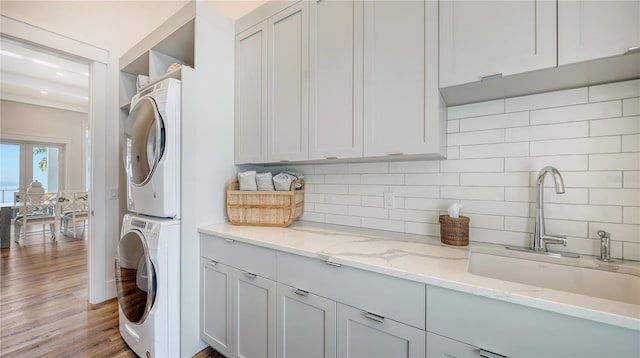 washroom featuring cabinets, stacked washer and dryer, light wood-type flooring, and sink