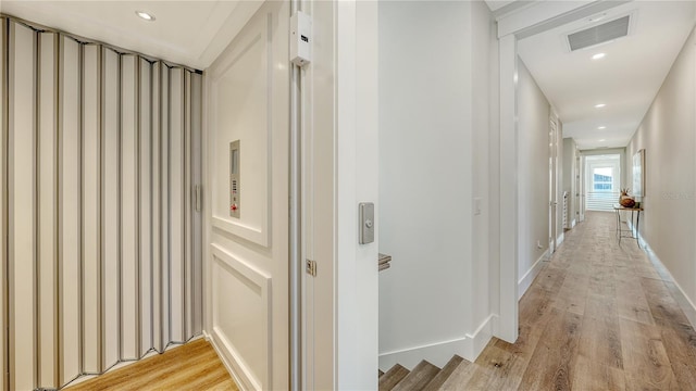 corridor with light hardwood / wood-style floors and elevator