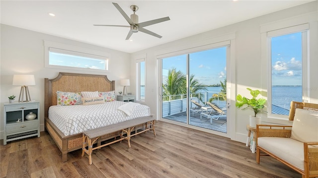 bedroom with access to exterior, ceiling fan, a water view, and hardwood / wood-style flooring