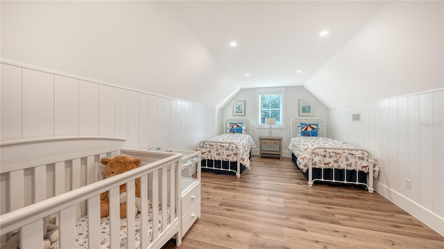 bedroom featuring light wood-type flooring, lofted ceiling, and a nursery area