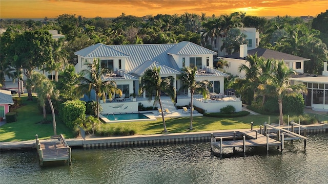 back house at dusk with a balcony, a patio area, and a water view