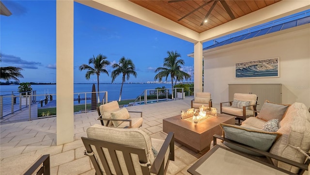 patio terrace at dusk featuring a water view, an outdoor living space with a fire pit, and ceiling fan