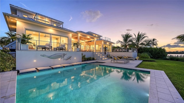 pool at dusk with a patio and a lawn