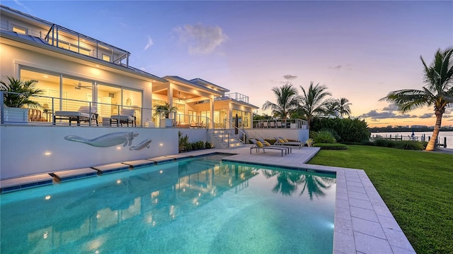 pool at dusk featuring a lawn and a patio