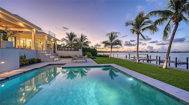 pool at dusk with a lawn, a water view, a dock, and a patio