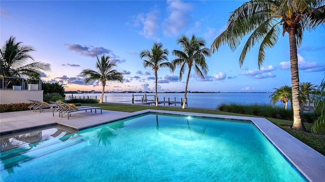 pool at dusk with a patio, a water view, and a dock