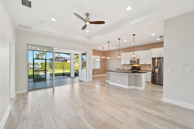 kitchen with white cabinets, ceiling fan, a tray ceiling, decorative light fixtures, and stainless steel appliances