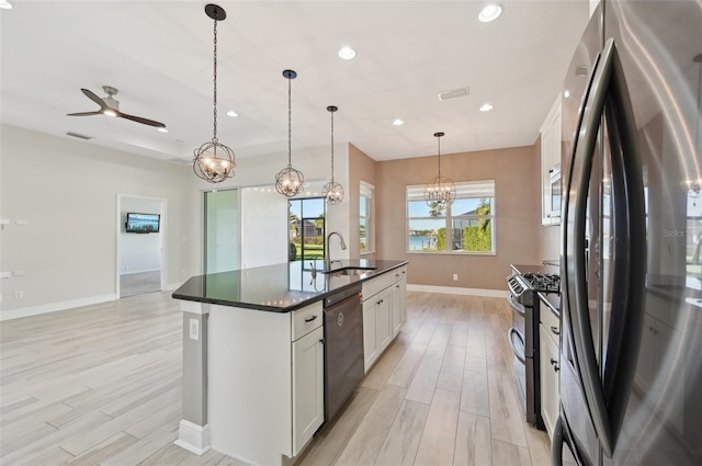 kitchen with stainless steel appliances, sink, a center island with sink, white cabinetry, and hanging light fixtures