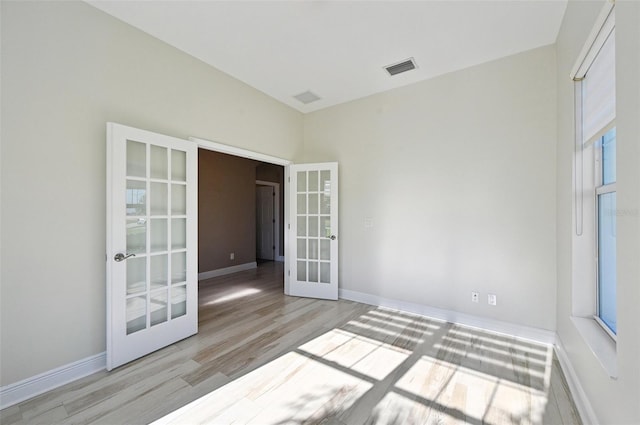 empty room featuring a healthy amount of sunlight, light hardwood / wood-style flooring, and french doors