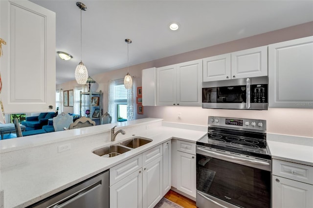 kitchen with kitchen peninsula, appliances with stainless steel finishes, sink, white cabinets, and hanging light fixtures