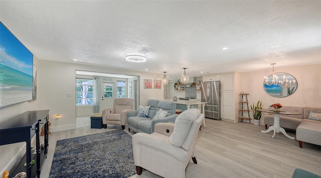 living room with a chandelier, a textured ceiling, and light wood-type flooring