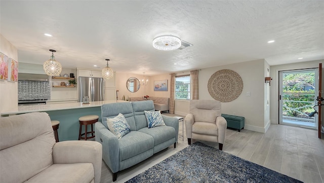 living room with light hardwood / wood-style floors, a textured ceiling, and an inviting chandelier