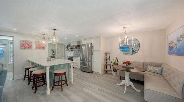 kitchen with a kitchen bar, appliances with stainless steel finishes, breakfast area, white cabinets, and hanging light fixtures