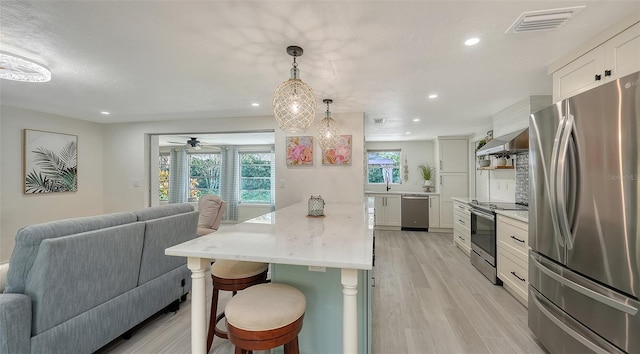 kitchen with a kitchen breakfast bar, stainless steel appliances, decorative light fixtures, light hardwood / wood-style floors, and white cabinetry