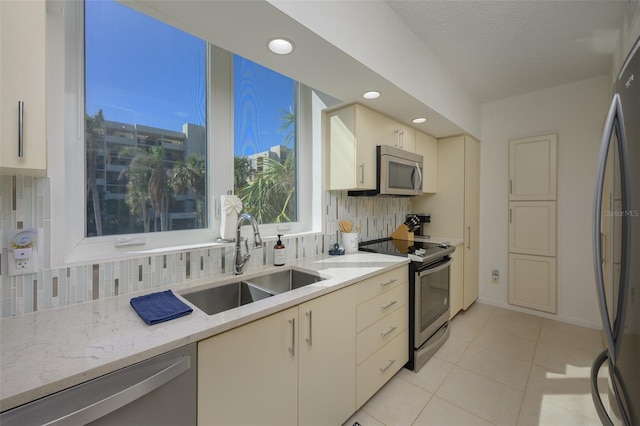 kitchen featuring backsplash, sink, light stone countertops, appliances with stainless steel finishes, and light tile patterned flooring