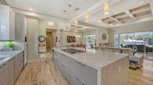 kitchen with a notable chandelier, stainless steel gas stovetop, coffered ceiling, decorative light fixtures, and a large island