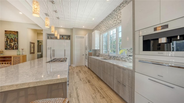 kitchen with sink, hanging light fixtures, light stone countertops, tasteful backsplash, and light hardwood / wood-style floors