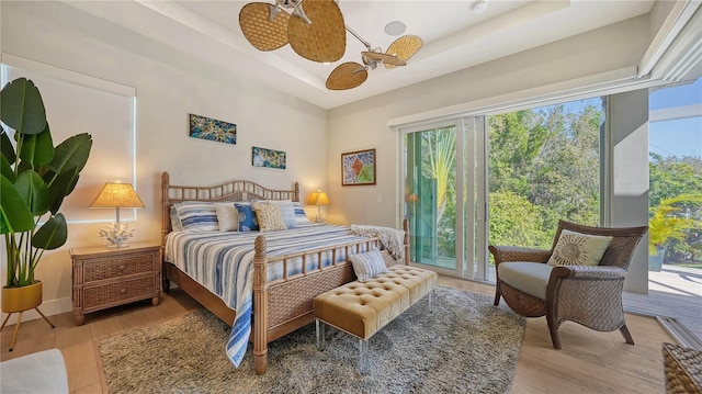 bedroom with ceiling fan, light wood-type flooring, access to outside, and a tray ceiling