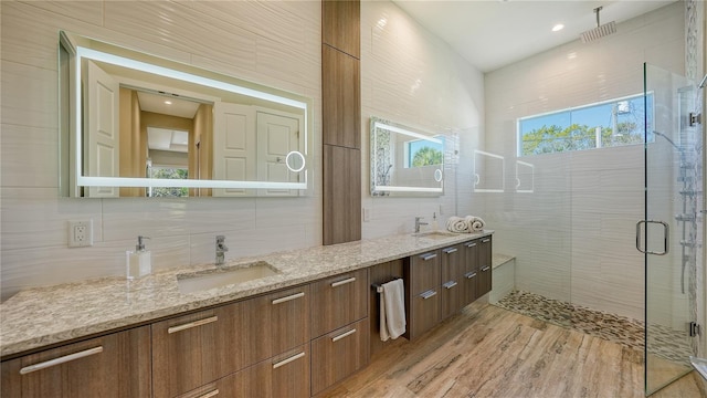 bathroom featuring vanity, wood-type flooring, a shower with shower door, and tile walls