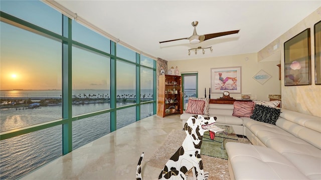 living room featuring expansive windows, ceiling fan, and a water view