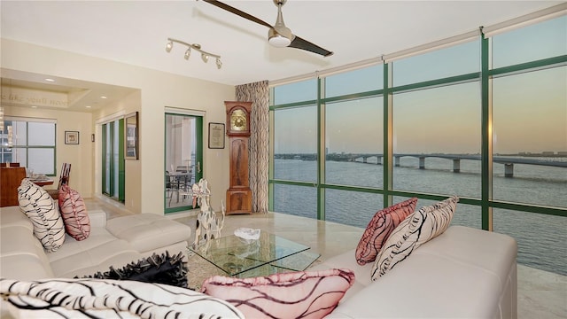 living room featuring floor to ceiling windows, ceiling fan, and a water view