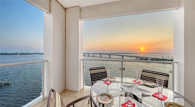 balcony at dusk featuring a water view