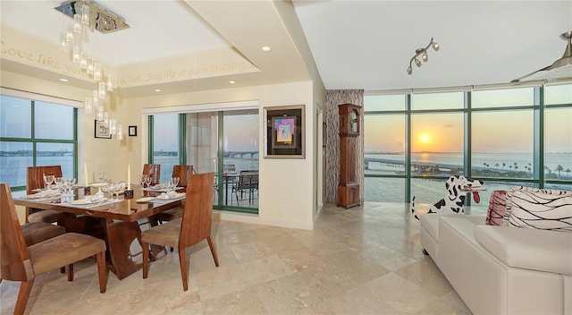 dining room featuring a tray ceiling, a water view, and a wall of windows