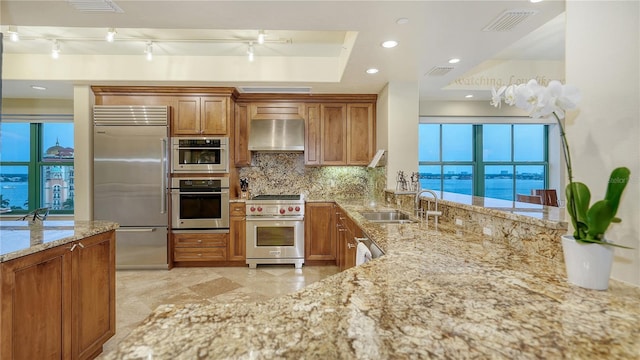 kitchen with light stone countertops, backsplash, wall chimney exhaust hood, and high quality appliances