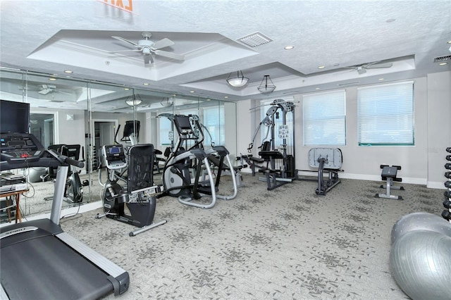 gym featuring a tray ceiling, ceiling fan, and ornamental molding