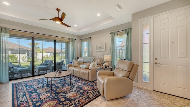 living room with a wealth of natural light, a raised ceiling, ceiling fan, and light tile patterned flooring