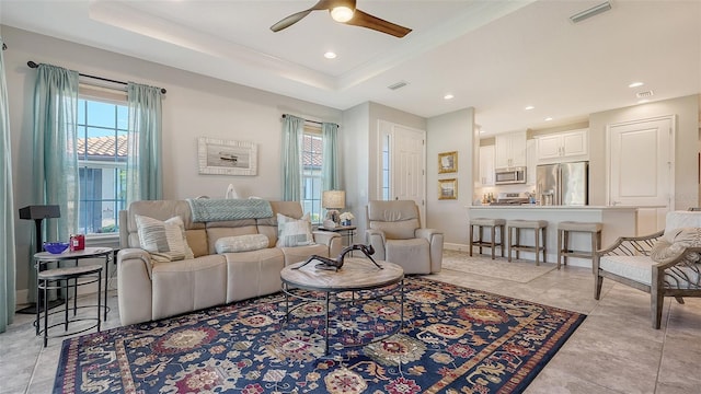 living room featuring a raised ceiling, ceiling fan, and light tile patterned floors