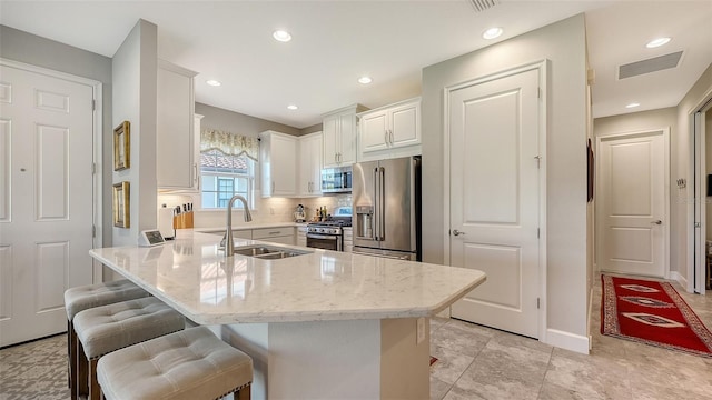 kitchen with light stone countertops, a breakfast bar, stainless steel appliances, sink, and white cabinets