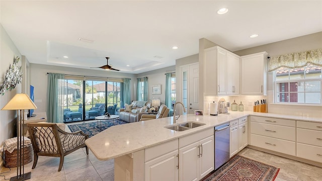 kitchen featuring ceiling fan, dishwasher, sink, kitchen peninsula, and a tray ceiling