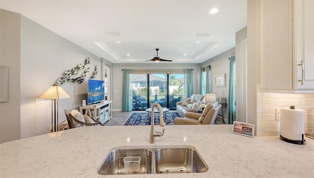 kitchen with a tray ceiling, light stone counters, sink, and ceiling fan