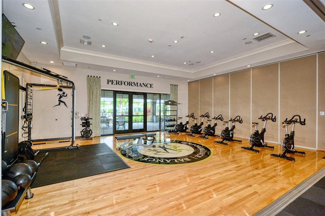 workout area with a raised ceiling, french doors, and light wood-type flooring