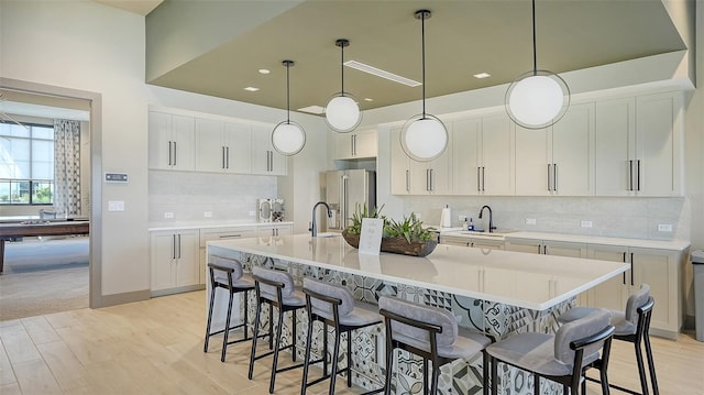 kitchen with white cabinets, decorative light fixtures, a large island with sink, and high quality fridge