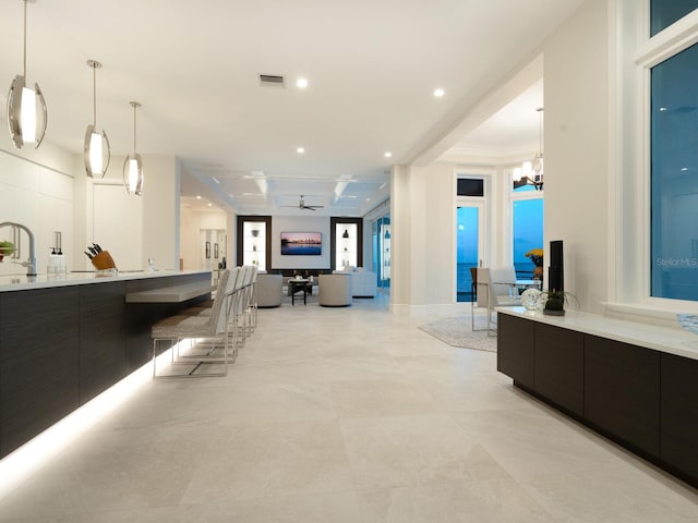 bar with pendant lighting, ceiling fan with notable chandelier, dark brown cabinetry, and sink