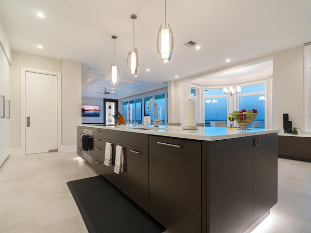 kitchen featuring a kitchen island with sink, ceiling fan with notable chandelier, sink, hanging light fixtures, and dark brown cabinetry