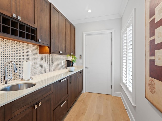 kitchen with backsplash, sink, light hardwood / wood-style flooring, ornamental molding, and light stone counters