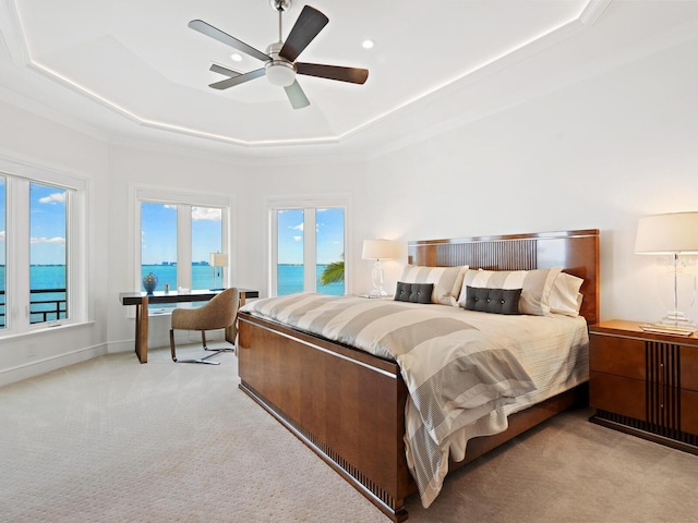 carpeted bedroom featuring a water view, a raised ceiling, and ceiling fan