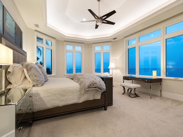 carpeted bedroom with ceiling fan and a raised ceiling