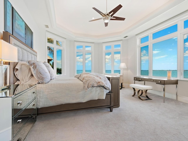 bedroom featuring a tray ceiling, ceiling fan, a water view, and light carpet