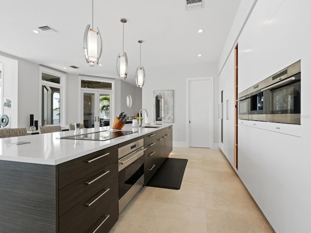 kitchen with a large island with sink, oven, sink, hanging light fixtures, and dark brown cabinetry