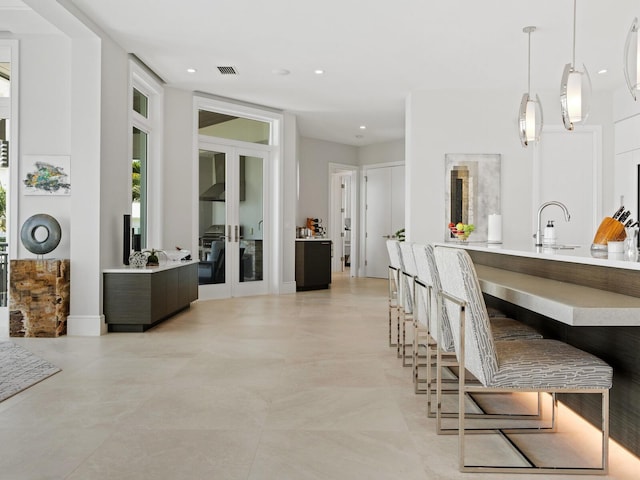 kitchen with french doors, hanging light fixtures, wall chimney exhaust hood, and sink