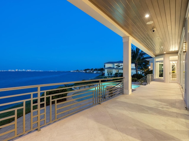 patio terrace at dusk featuring a water view and a balcony